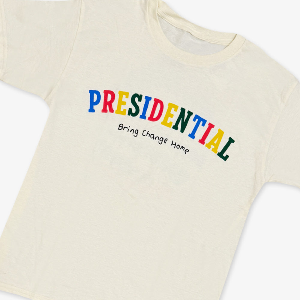 The Presidential Bring Change Home Youth T-Shirt is an off-white tee featuring PRESIDENTIAL in bold, colorful letters with Bring Change Home below in black—celebrating the Obama Foundation’s mission for positive change.