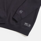 A close-up of the Obama Presidential Center Chicago Script Sweatshirt shows the number 44 stitched on the sleeve and a label with text and numbers, including 44, near the hem. The dark sweatshirt is set against a white background.