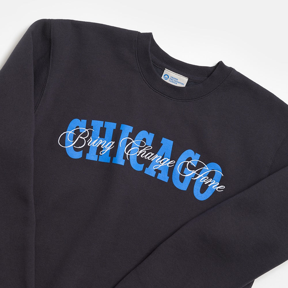 The Obama Presidential Center Chicago Script Sweatshirt is a black sweatshirt with CHICAGO in bold blue letters and "Bring Change Home" in white script, reflecting the center’s inspiring spirit.