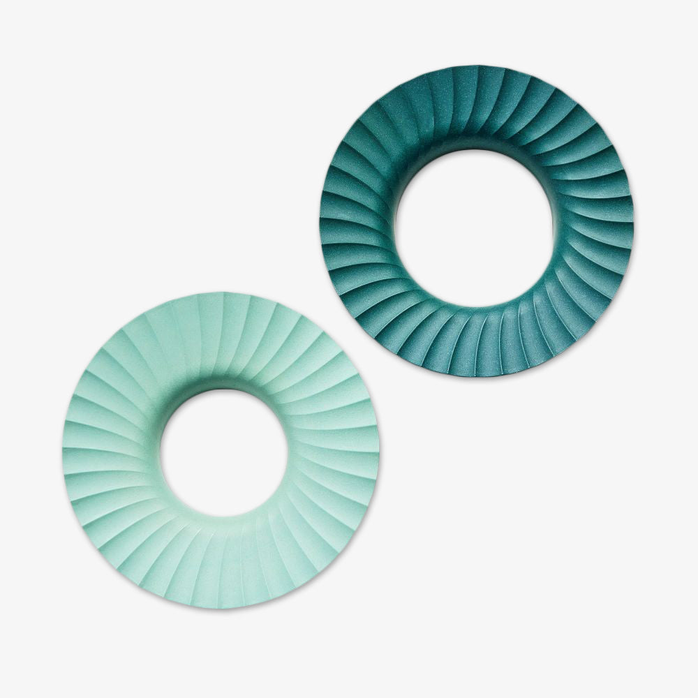 Two donut-shaped Produce Keepers, one in light mint green and one in dark teal with spiral ridges, sit on a white background. These eco-friendly containers help maintain your produce's freshness.