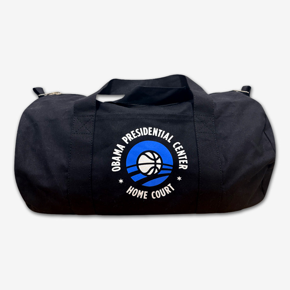 The Obama Presidential Center Home Court Duffel Bag is a black cotton canvas bag with a basketball logo and “Obama Presidential Center Home Court” in white and blue, featuring two handles and a zipper closure.