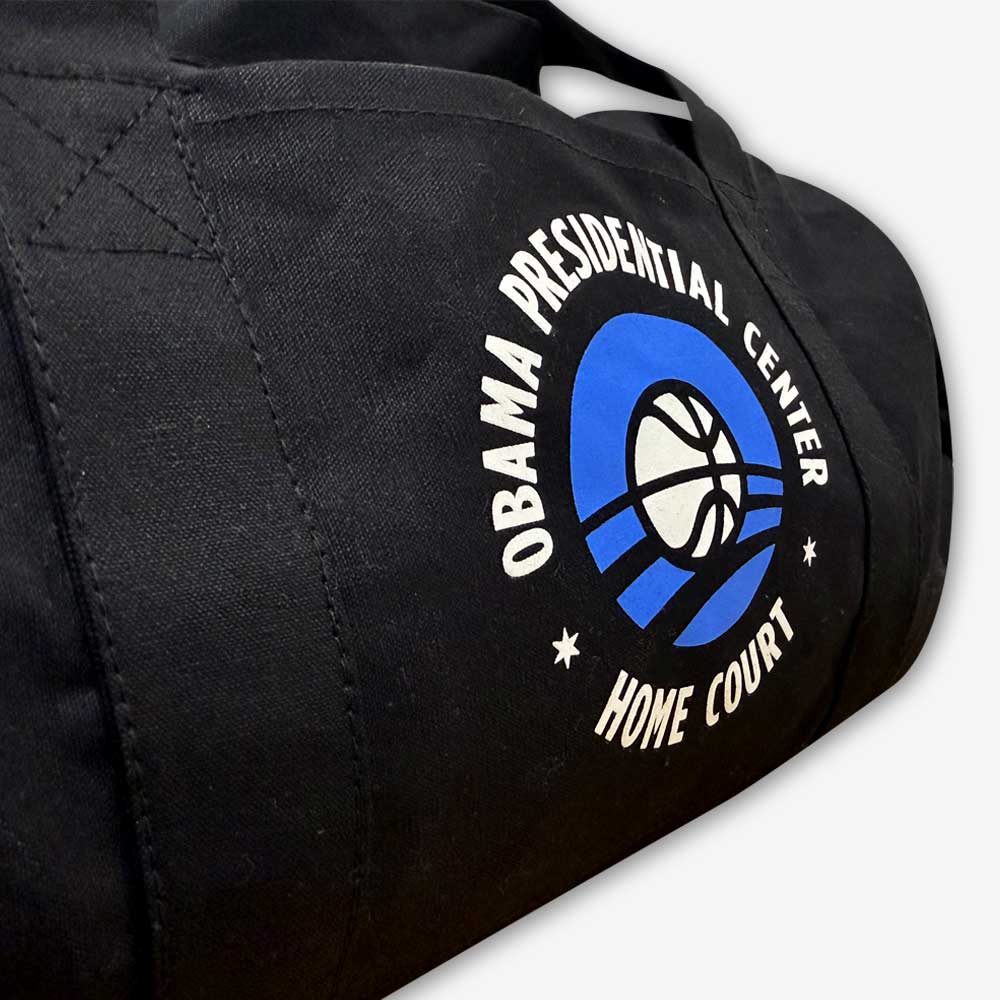 The Obama Presidential Center Home Court Duffel Bag features black cotton canvas with a basketball and blue arcs logo—an official Obama Foundation item.