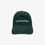 The Obama Presidential Center Community Cap is dark green, shown from the back with an adjustable strap and a light blue embroidered circular logo of curved sunrise or sunset lines—an official cap.