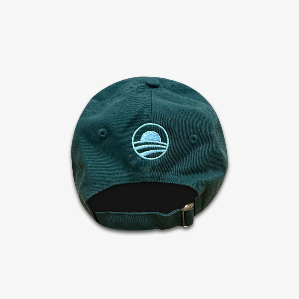 The Obama Presidential Center Community Cap is dark green, shown from the back with an adjustable strap and a light blue embroidered circular logo of curved sunrise or sunset lines—an official cap.