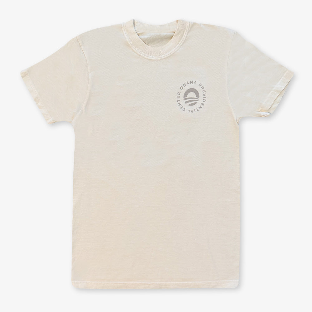 The Obama Presidential Center Hope to Action T-Shirt in Ivory features a small circular logo and emblem on the upper left chest, displayed flat on a white background.