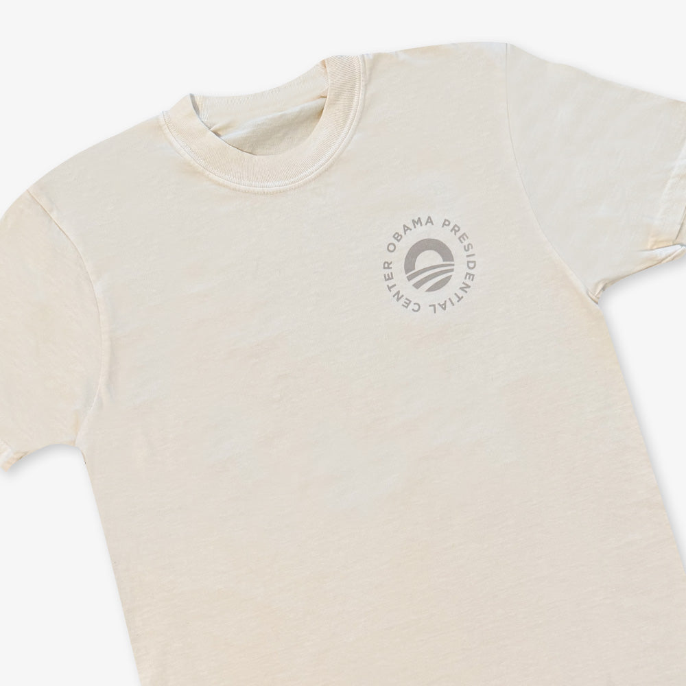 The Obama Presidential Center Hope to Action T-Shirt in ivory features an abstract circular logo with "Obama Presidential Center" text on the left chest for an inspirational look.