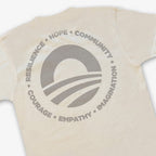 The Obama Presidential Center Hope to Action T-Shirt in ivory features a large circular sunrise logo on the back with the words Resilience, Hope, Community, Imagination, Empathy, and Courage.