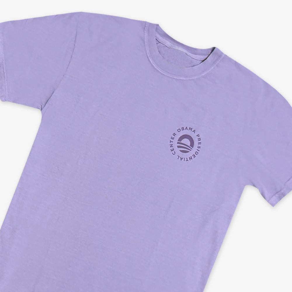 The Obama Presidential Center Hope to Action T-shirt is a lavender short-sleeve shirt with a small circular “O” logo on the left chest, displayed flat against a white background.