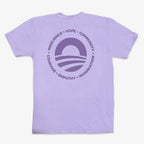 The Obama Presidential Center Hope to Action T-shirt is light purple with a large circular logo on the back, featuring a sun and stripes, surrounded by "RESILIENCE • HOPE • COMMUNITY • COURAGE • EMPATHY • IMAGINATION" in purple text.
