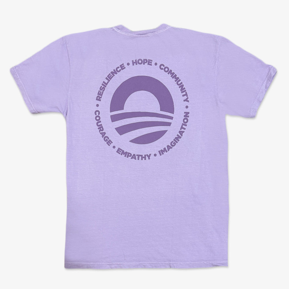 The Obama Presidential Center Hope to Action T-shirt is light purple with a large circular logo on the back, featuring a sun and stripes, surrounded by "RESILIENCE • HOPE • COMMUNITY • COURAGE • EMPATHY • IMAGINATION" in purple text.