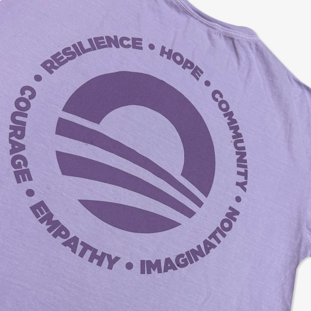 The Obama Presidential Center Hope to Action T-shirt is a lavender tee with a large circular stylized horizon graphic and bold words—RESILIENCE, HOPE, COMMUNITY, NATION, IMAGINATION, EMPATHY, COURAGE—for inspiring wear.