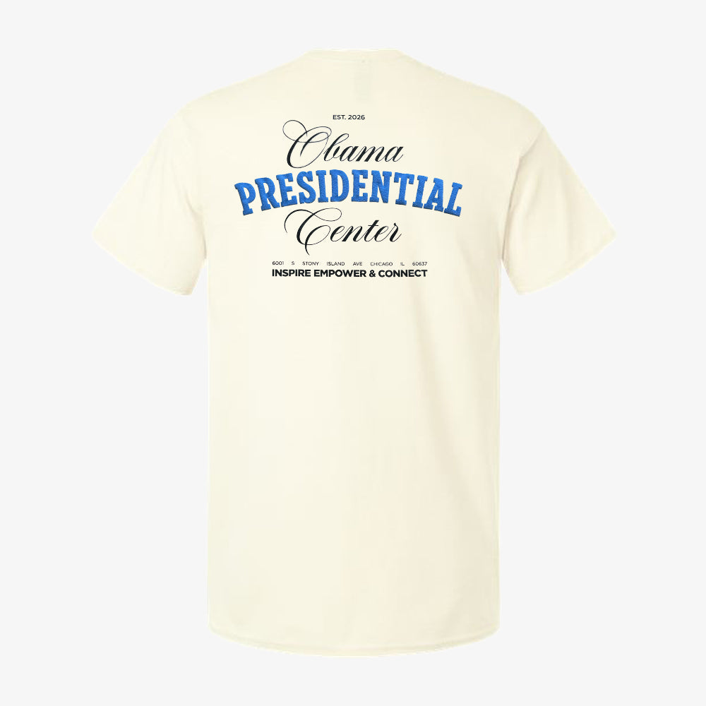The back of the Obama Presidential Center Script T-shirt in ecru features blue and black text displaying “Obama Presidential Center” and “Inspire Empower & Connect,” includes the establishment year, city names like Chicago South Side, and a phrase about inspiration.