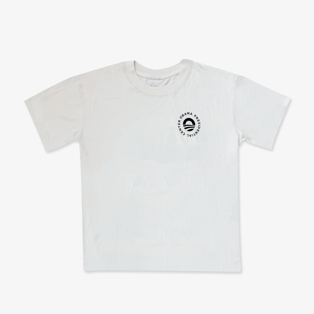 The Obama Presidential Center Home Court T-shirt is a plain white short-sleeve tee with a small black circular logo and "Obama Beach" and "Brasil" text around a wave icon on the upper left chest—ideal for casual style.