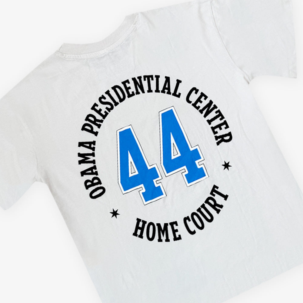 The Obama Presidential Center Home Court T-shirt is white with "OBAMA PRESIDENTIAL CENTER HOME COURT" in black lettering on the front and a bold blue number 44 printed on the back.