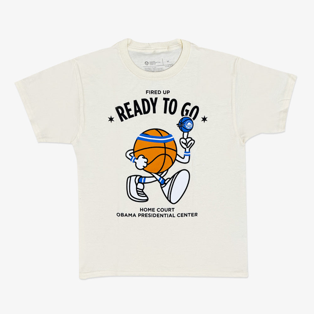 The Obama Presidential Center Home Court Youth T-Shirt is cream-colored and features a cartoon basketball character with a foam finger and microphone, plus the text "Fired Up Ready To Go" and "Home Court Obama Presidential Center.