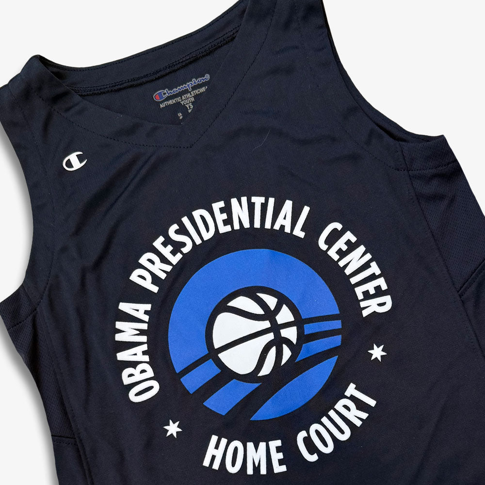 Obama Presidential Center Home Court Youth Jersey in navy blue, featuring "Obama Presidential Center Home Court" encircling a basketball graphic with blue curved lines and a Champion logo on the left shoulder.