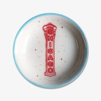 The Chicago Sign Trinket Dish is a handmade round white porcelain dish with a light blue rim, red speckles, and an illustration of the iconic vertical red Chicago Theatre sign at the center.