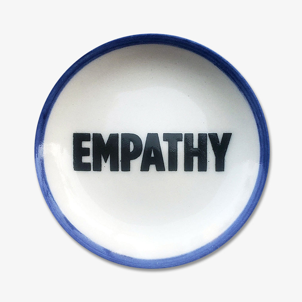 The Empathy Trinket Dish is a handmade porcelain dish with a blue rim and “EMPATHY” in bold black letters—a unique piece supporting a Black-owned business.