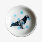 The Pigeon Trinket Dish is a small handmade porcelain dish with a black and white pigeon illustration and light blue polka dots—perfect as a unique Chicago gift.