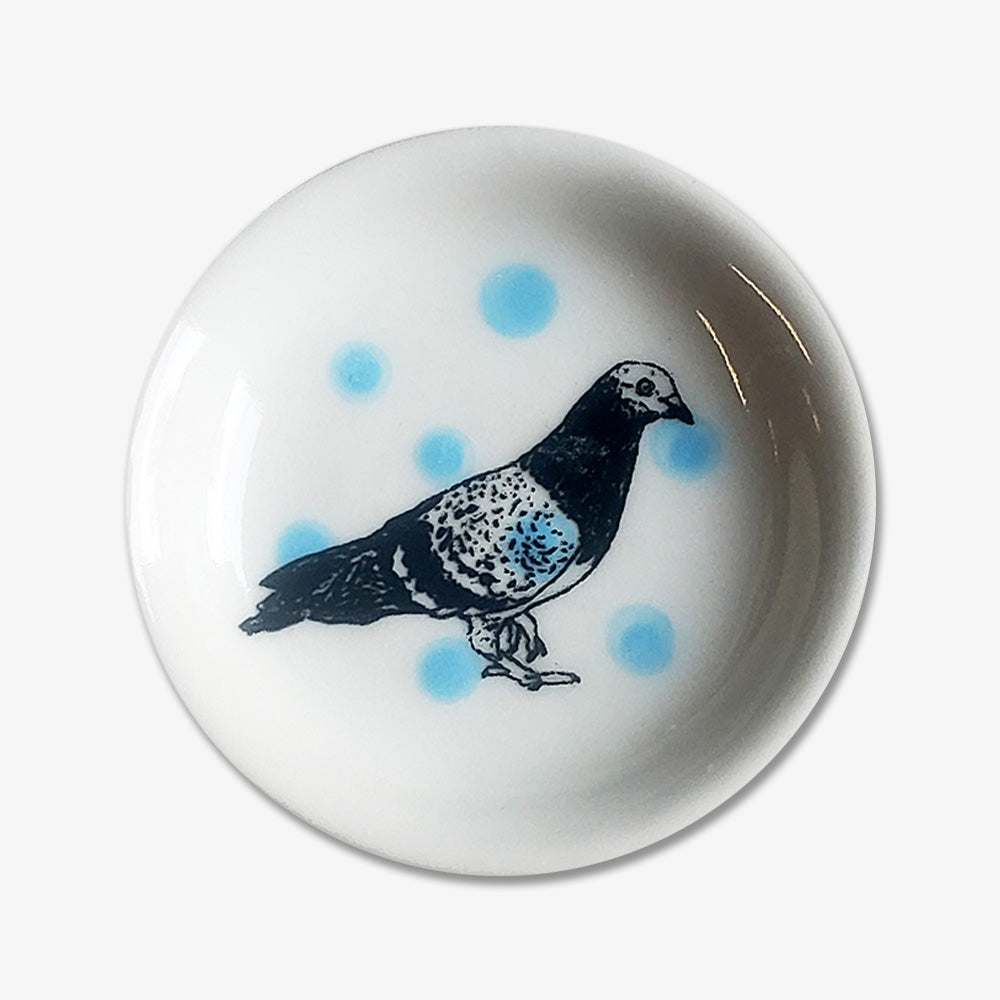 The Pigeon Trinket Dish is a small handmade porcelain dish with a black and white pigeon illustration and light blue polka dots—perfect as a unique Chicago gift.