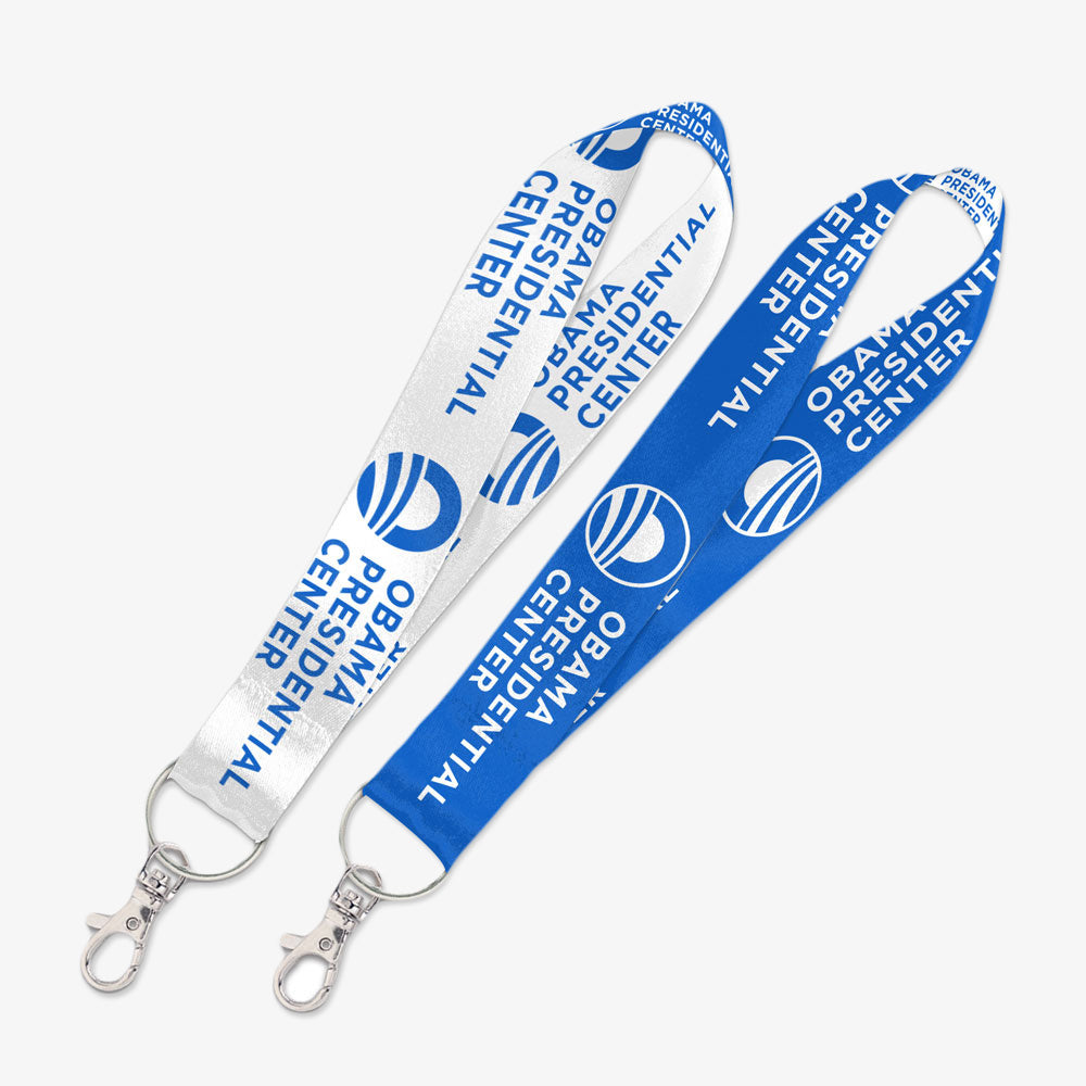 The Obama Presidential Center Key Strap comes in white or blue, each with the Center’s name and circular logo. Both feature a metal clasp and are shown on a light background. Official Obama Foundation merchandise.