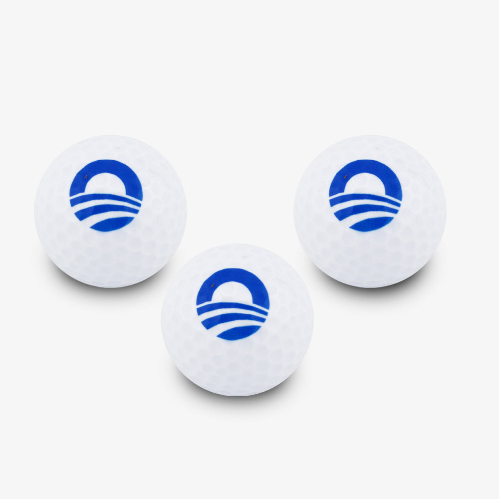 Three Obama Presidential Center Golf Balls, each white and marked with the Foundation’s blue “O” logo and stripes, are arranged in a loose triangle on a white background.