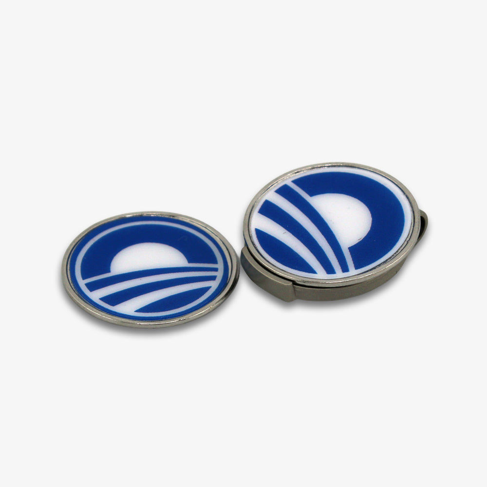 The Obama Presidential Center Hat Clip & Ball Markers feature two round pins with a blue and white rising sun design, displayed on a white background—ideal as stylish ball markers for any golf accessory set.