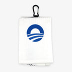 The Obama Presidential Center Golf Towel is a folded white towel with a blue stylized O logo and a black hanging clip—an essential golf accessory.