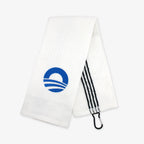 The Obama Presidential Center Golf Towel features a blue circular wave/sunrise logo, black-and-white striped loop, and black carabiner for easy hanging—a unique addition to any golf accessories collection. Plain white background.