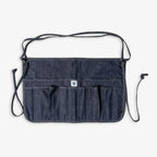 The Waist Apron, made from 100% cotton dark denim, features multiple front pockets and long adjustable straps, shown laid flat on a light background.