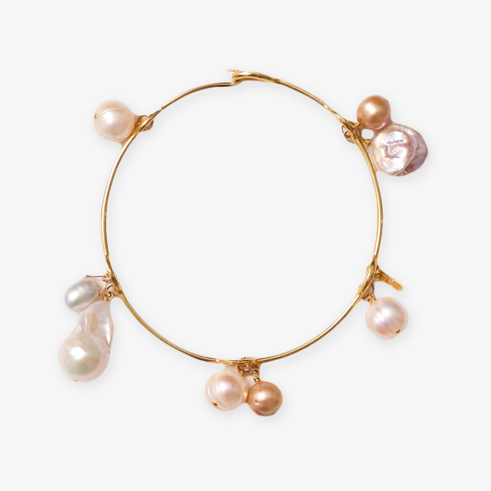 The Gold Crown Pearl Bangle features an elegant gold band decorated with assorted freshwater pearls and pearl-like charms in various sizes and colors, beautifully displayed on a white background.