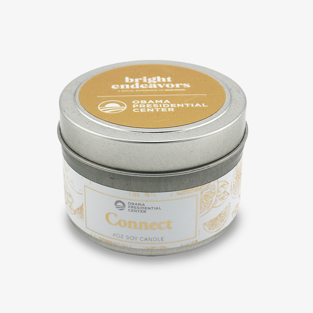 A small silver tin with a gold lid, labeled "bright endeavors" and "Obama Presidential Center." Side label: Connect Sprig Candle 4oz hand-poured, citrus slice illustrations—part of the Sugared Grapefruit Candle by Obama Foundation.