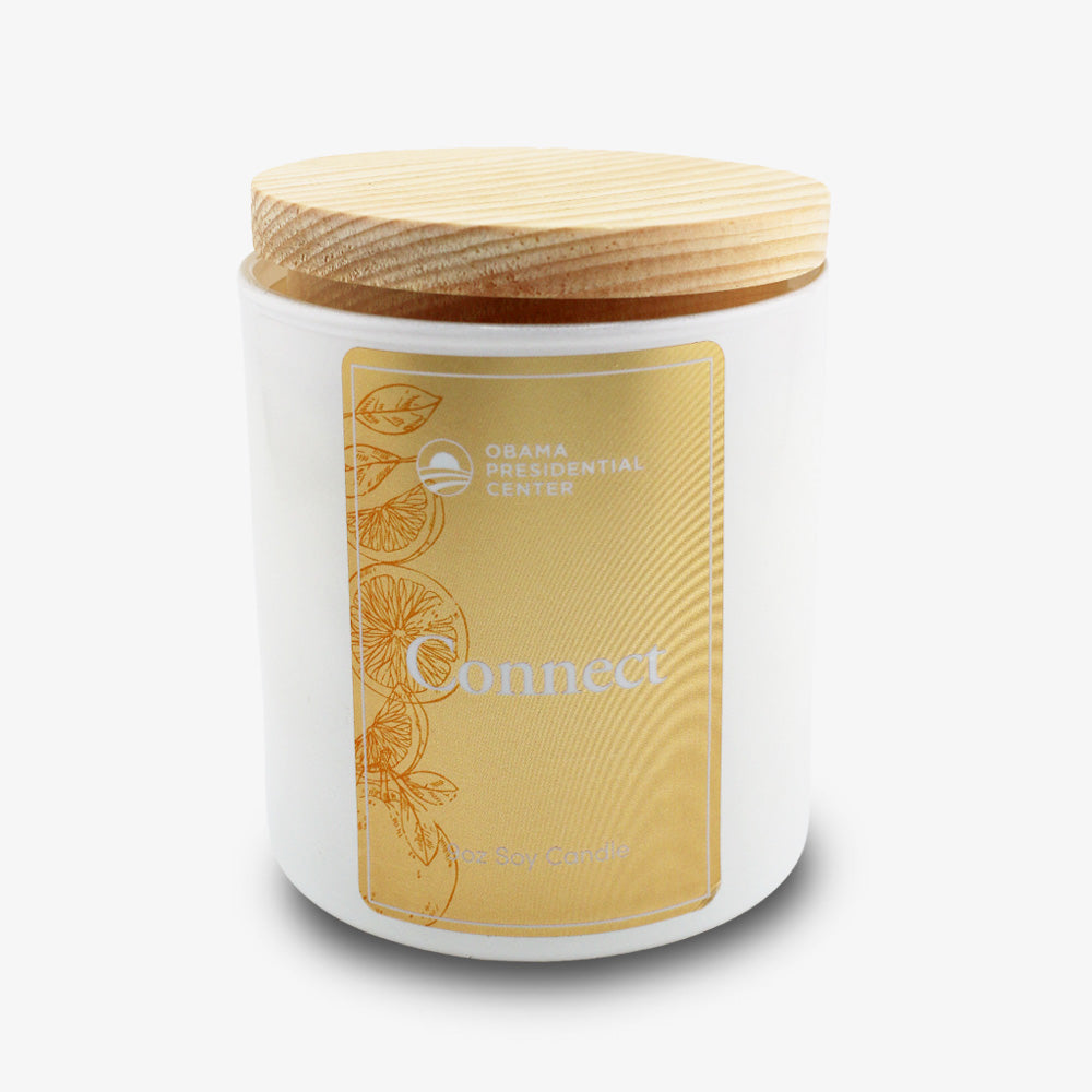 A white jar with a wooden lid, yellow label reading "Connect Sprig Candle 9 oz. by Bright Endeavors," and citrus slice art—this sugared grapefruit candle supports the Obama Foundation’s Obama Presidential Center.