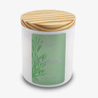 A white hand-poured candle jar with a light wooden lid and a green label reading Empower Sprig Candle 9 oz., featuring a botanical illustration on the left side of the label.