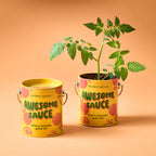 Two yellow cans of Awesome Sauce Grow Kit sit side by side—one closed, one with a green sprout. With playful designs on an orange background, these reusable planters are perfect for fun home gardening.
