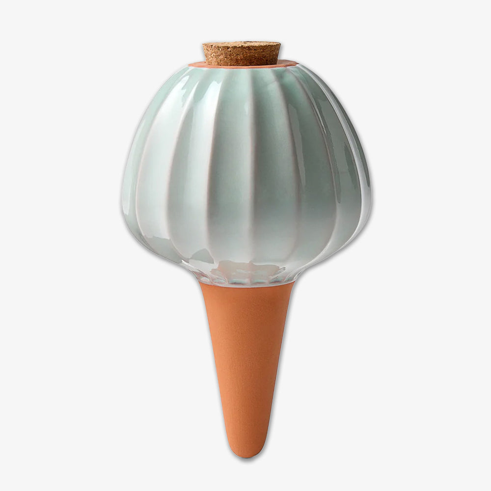 The Terracotta Watering Bulb features a round, light green ribbed ceramic top with a cork stopper, tapering to a pointed, unglazed terracotta spike for easy and efficient garden hydration inspired by ancient irrigation.