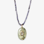 The Beaded Seed Gemstone Pendant Necklace features small faceted purple beads and an oval pendant with a translucent green stone, clear center gemstone, and gold detailing—an elegant piece that highlights artisan craftsmanship.