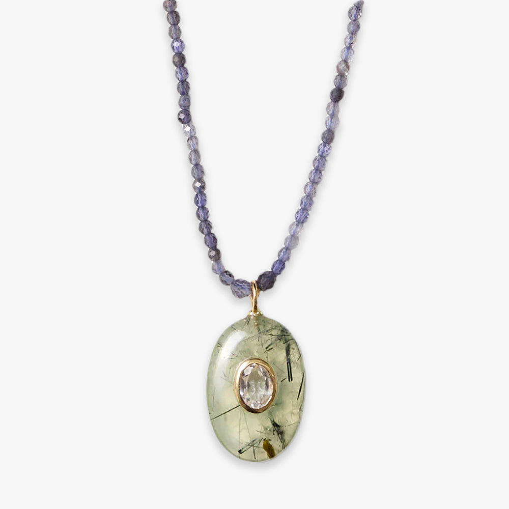 The Beaded Seed Gemstone Pendant Necklace features small faceted purple beads and an oval pendant with a translucent green stone, clear center gemstone, and gold detailing—an elegant piece that highlights artisan craftsmanship.