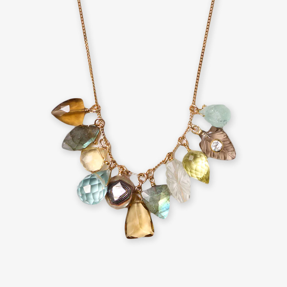 The Gemstone Charm Mix Necklace is a hand-crafted, sustainable artisan piece featuring gold with multiple leaf- and drop-shaped gemstone pendants in blue, green, yellow, brown, and clear hues.