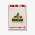The Pigeon Pin is a gold-outlined enamel pin with a red heart and green Chicago street sign, displayed on a card labeled ENAMEL PIN with "express yourself" in red.