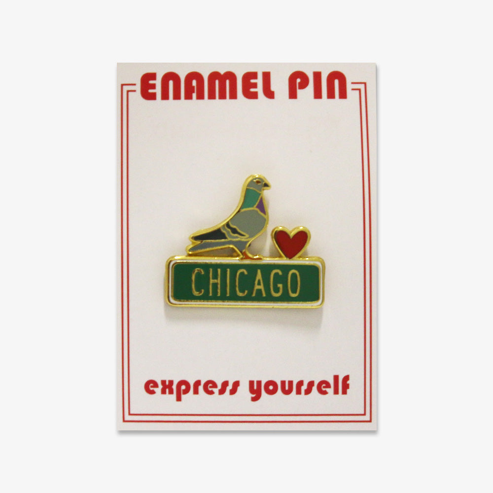 The Pigeon Pin is a gold-outlined enamel pin with a red heart and green Chicago street sign, displayed on a card labeled ENAMEL PIN with "express yourself" in red.