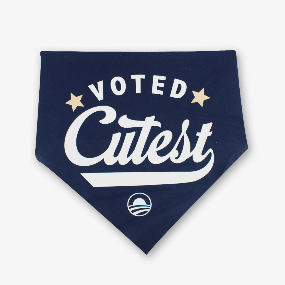 The Voted Cutest Kerchief is a navy dog bandana featuring bold white "Voted Cutest" text, two gold stars, and a small circular rising sun logo—an adorable accessory for your pup.