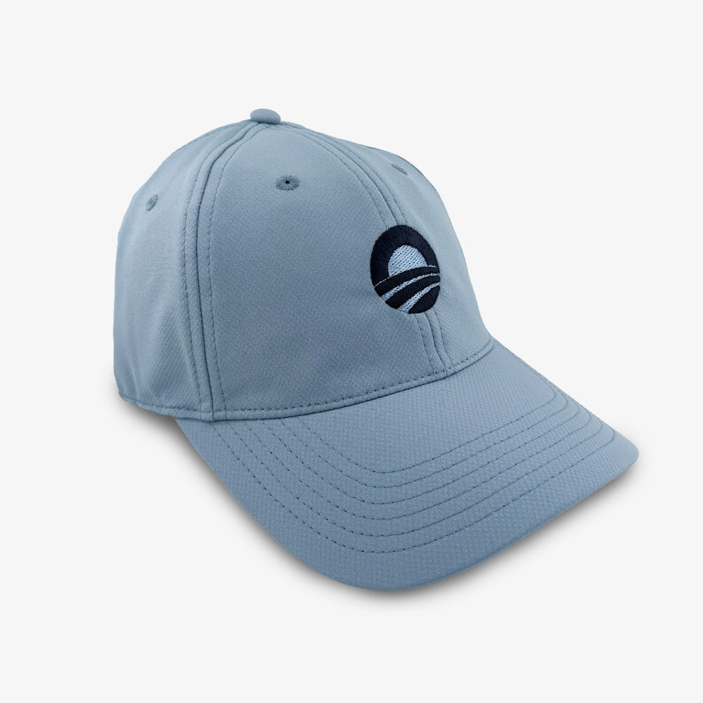 Slate blue performance golf cap with a curved brim, featuring a round embroidered logo of a stylized "O" and sunrise design on the front. Displayed against a plain white background, the Obama Presidential Center Golf Cap - Slate is the perfect accessory for supporters of the Obama Foundation.
