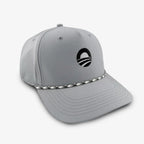 The Obama Presidential Center Golf Cap - Grey features a black circular logo on the front and a distinctive black-and-white braided rope along the base of the crown. Inspired by the Obama Presidential Center cap collection, this light gray performance cap stands out against a plain white background.