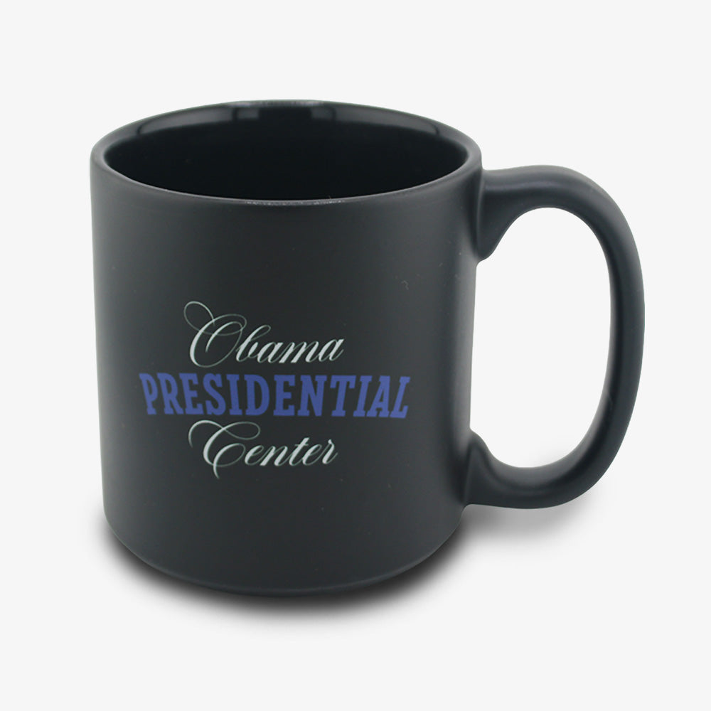 The Obama Presidential Center Script Mug is a matte black ceramic mug featuring "Obama Presidential Center" in white and blue script—an ideal choice for supporters of the Obama Foundation.