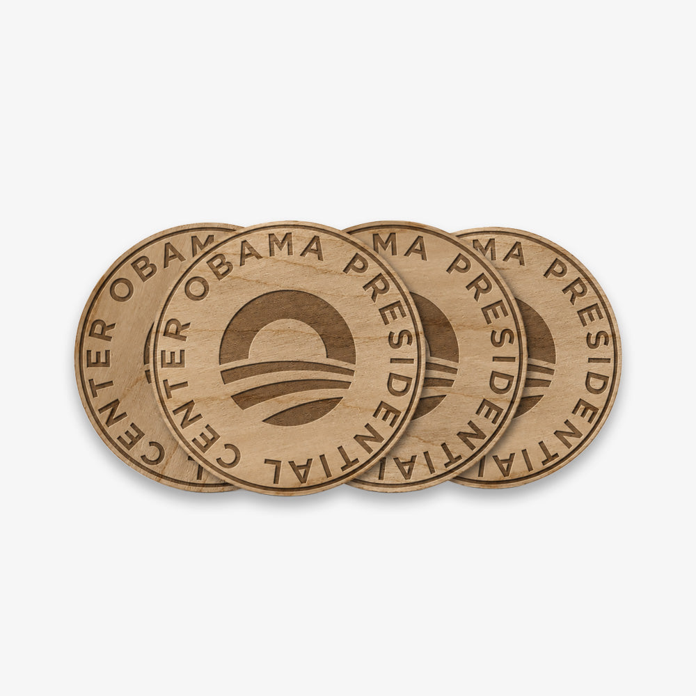 The Obama Presidential Center Coaster Set includes four round wood coasters with the center’s logo and “Obama Presidential Center” engraved around the edge, shown partially overlapping each other.