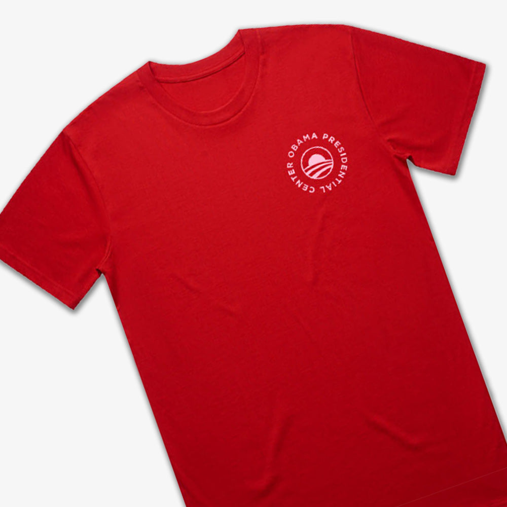 The Obama Presidential Center Hope to Action T-shirt – Sunset is a vibrant red tee featuring a small white circular logo with “Obama Presidential Center” and a stylized O on the left chest—a bold statement from the Obama Foundation.