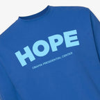 The Obama Presidential Center Hope Sweatshirt - Royal Blue features “HOPE” in large light blue letters and “Obama Presidential Center” in smaller text underneath.
