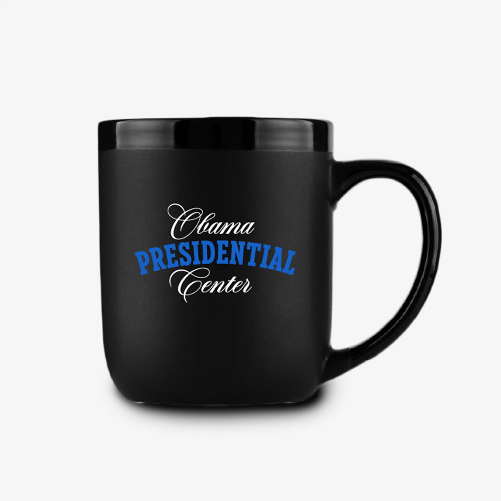 Introducing the Obama Presidential Center Script Mug: a matte black ceramic mug featuring “Obama Presidential Center” in white and blue script on the front, set against a clean white background—an official Obama Foundation item ideal for any collection.