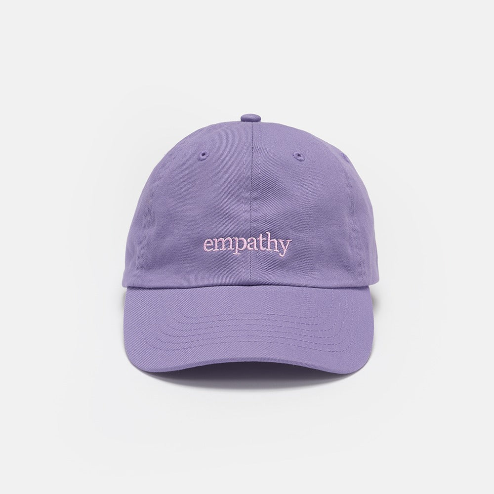 The Obama Presidential Center Empathy Cap is a lavender baseball cap with "empathy" embroidered in white lowercase letters on the front, shown against a plain white background.